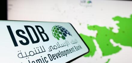 Cellphone with logo of Islamic Development Bank (IsDB) on screen in front of website. Focus on center-left of phone display.