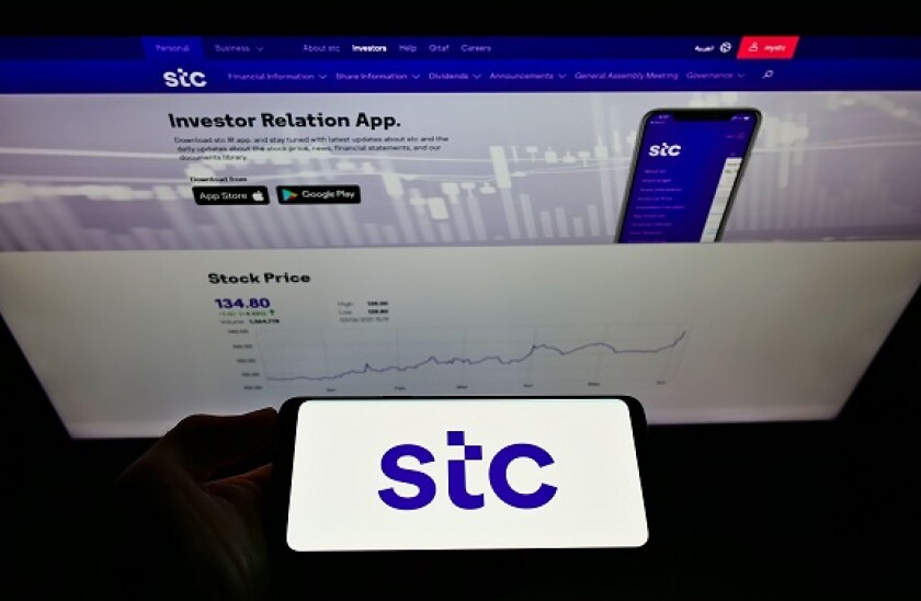 Person holding smartphone with logo of Arabian carrier Saudi Telecom Company (STC) on screen in front of website. Focus on phone display.
