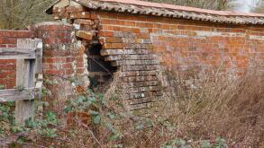 a crumbling red brick wall around a farm yard in need of repair