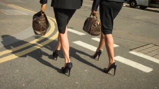 A pair of identically dressed business women walking down the road in high heels.