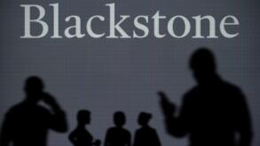 The Blackstone logo is seen on an LED screen in the background while a silhouetted person uses a smartphone in the foreground (Editorial use only)