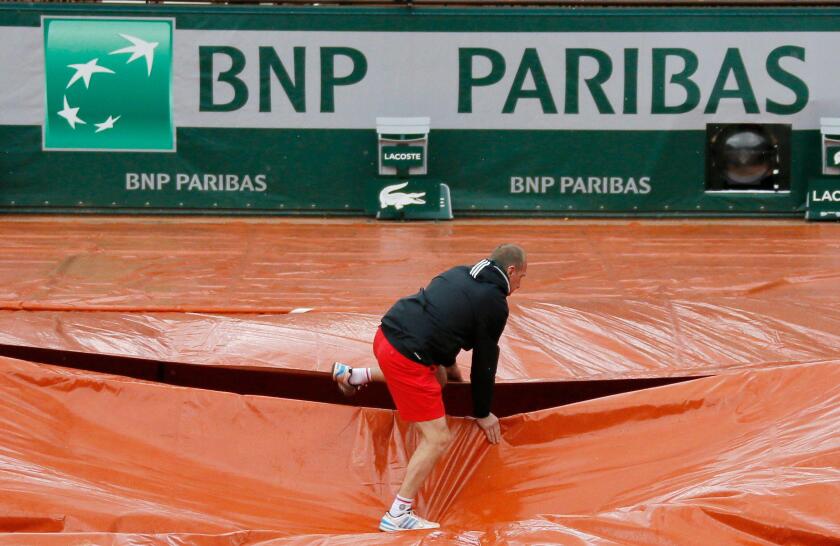 A grounds crew member covers the clay court from rain near the logo of BNP Paribas during the French Open tennis tournament at Roland Garros in Paris May 30, 2014. Shares in France's biggest bank BNP Paribas fell sharply on Friday on concerns a possible f