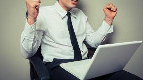 A young businessman is sitting in an office chair and is getting excited about his laptop