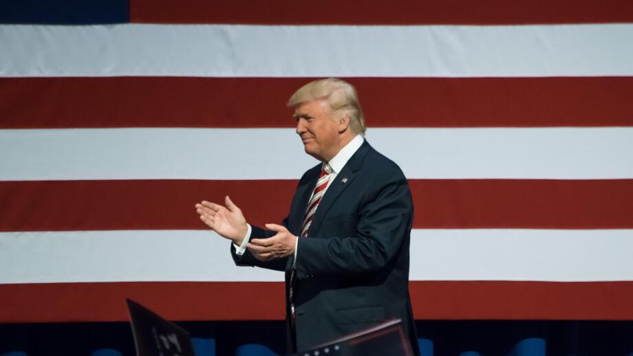 Republican Presidential Nominee Donald Trump walking on stage applauding the crowd near the American Flag.