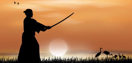 Samurai stands with a sword in his hands against the backdrop of a sunny sunset. Japanese landscape.