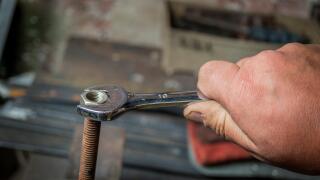 worker hand tightening or loosening a nut of a rusty bolt with a wrench on white background