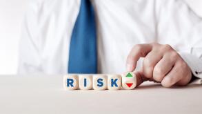 Businessman hand turns a wooden cube with the arrows symbolizing the risk level is high or low.
