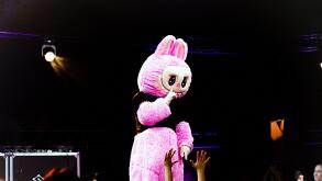 Labubu cheering crowd with bright lights, vivid neon illumination enhances lively performance atmosphere, energetic scene featuring enormous pink