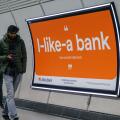 Commuters walk past an Advert for Allica Bank on wall of London railway station  London UK