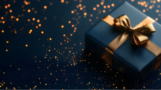 A dark blue holiday gift wrapped in a gold ribbon, set against a blue and sparkly background