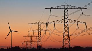 Silhouettes of a wind turbine and electric power posts during sunset