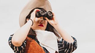 cute chinese cowgirl while looking at the horizon with binoculars on a wild west farm