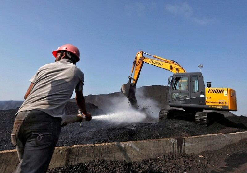 A worker sprays water over piles of coal as a bulldozer shifts coal at Mundra Port Coal Terminal in the western Indian state of Gujarat April 2, 2014. The way billionaire Indian infrastructure-builder Gautam Adani sees it, working with the government does