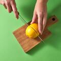 A woman's hands cut a yellow ripe lemon in half with knife on a wooden board on a green background. Top view.