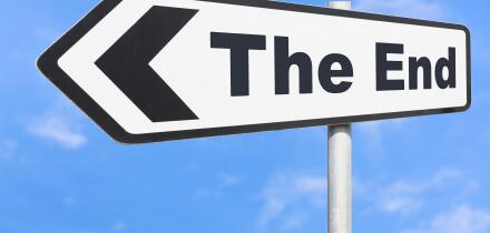 The End direction sign pointing to the left against blue sky.