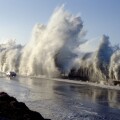 A huge storm surge wave dwarfs a car travelling on Highway 1 at Solimar Beach California
