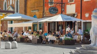 Restaurant piazza Italy, view in summer of a group of people dining outside a pizzeria in the scenic port of Chioggia, Comune of Venice, Italy