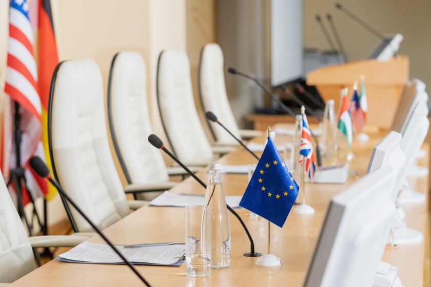 Row of microphones, flags, papers and other on long table in conference hall