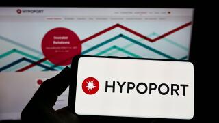 Person holding smartphone with logo of German technology company Hypoport SE on screen in front of website. Focus on phone display.