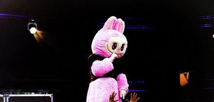 Labubu cheering crowd with bright lights, vivid neon illumination enhances lively performance atmosphere, energetic scene featuring enormous pink