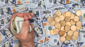 Conceptual financial image of a man clutching a wad of dollar bills over a background of multiple scattered new 100 dollar bills