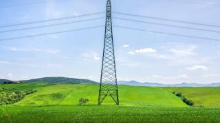 High voltage power line tower standing in a lush green field in Tuscany. Modern infrastructure in a rural spring landscape near Volterra, Italy