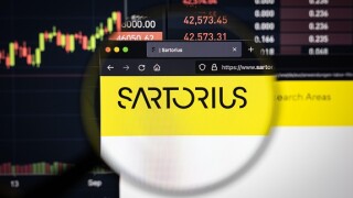 Sartorius company logo on a website with blurry stock market developments in the background, seen on a computer screen through a magnifying glass