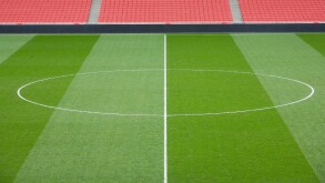 centre circle of a football pitch and bright red seating inside an empty football stadium.