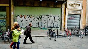 People walking past graphiti on a closed shop in the Via degli Orefici, Bologna, Italy