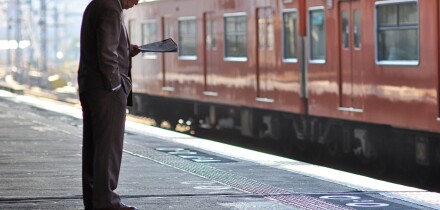 An elderly man reading a newspaper while waiting for a train.