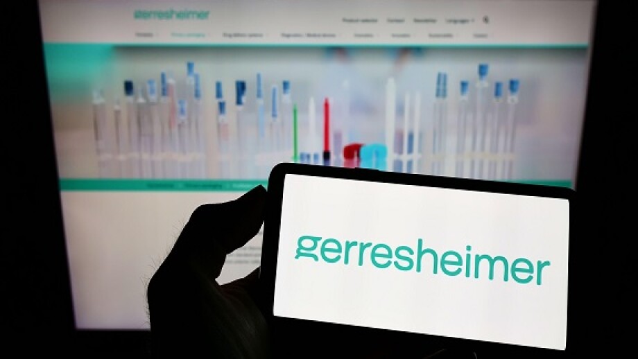 Person holding smartphone with logo of German packaging company Gerresheimer AG on screen in front of website. Focus on phone display.