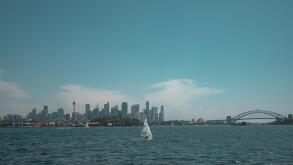 Wide angle view of the Sydney Harbour skyline featuring the CBD, Sydney Opera House, and Harbour Bridge with sailboats in the foreground.