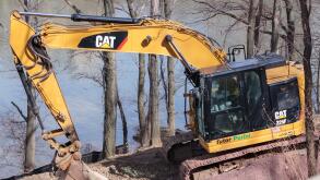 a cat 325f excavator bulldozer parked on the side of a hill on the Hudson River, by Caterpillar brand, with a Tutor Perini label, a major construction