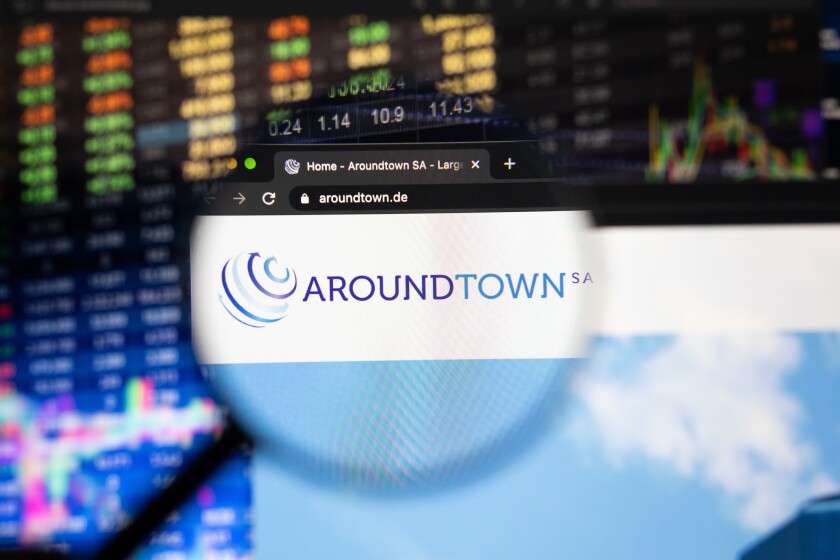 Aroundtown SA company logo on a website with blurry stock market developments in the background, seen on a computer screen through a magnifying glass