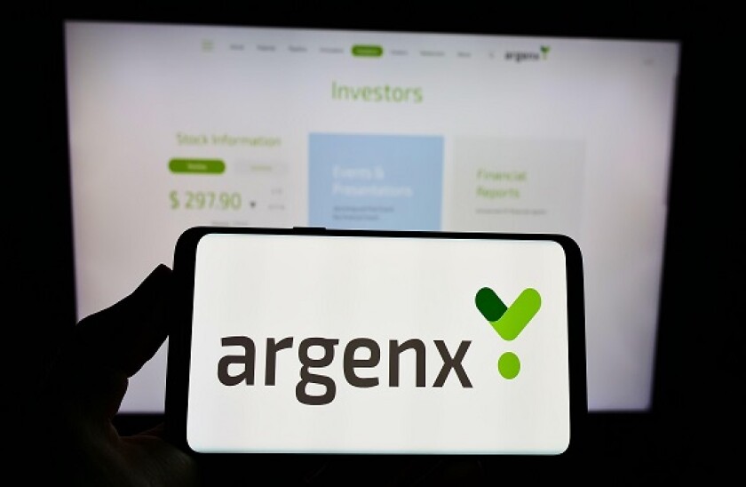 Person holding smartphone with logo of Dutch biotechnology company argenx SE on screen in front of website. Focus on phone display.