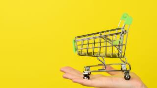 Empty shopping cart on female hand. Shopping theme. Small Trolley isolated on a bright yellow background. Consumer concept, Copy space.
