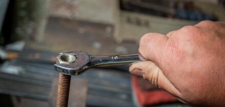worker hand tightening or loosening a nut of a rusty bolt with a wrench on white background