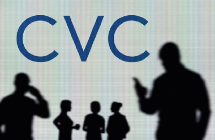 The CVC Capital Partners logo is seen on an LED screen in the background while a silhouetted person uses a smartphone (Editorial use only)