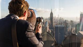 USA, New York City, man looking through coin-operated binoculars on Rockefeller Center observation deck