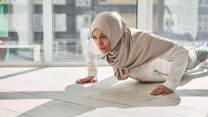 Determined Arab Muslim woman doing push-ups against the background of large windows at home on a beautiful sunny day. Home workout concept