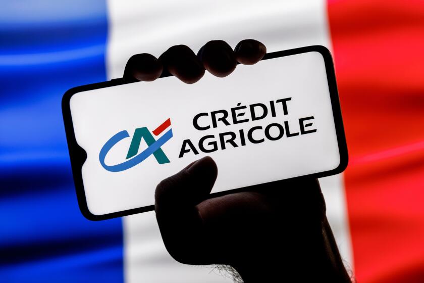 Smartphone with Credit Agricole bank logo in clenched hand on background of France flag