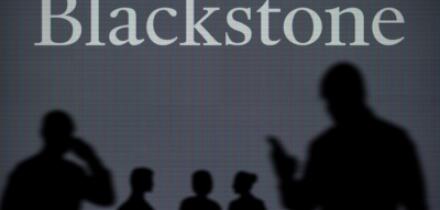 The Blackstone logo is seen on an LED screen in the background while a silhouetted person uses a smartphone in the foreground (Editorial use only)