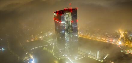 Aerial view of the European Central Bank skyscraper piercing through a sea of fog, its red lights ablaze against the muted city lights, Frankfurt am M