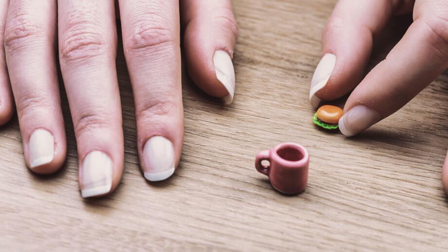 Miniature burger and coffee cup showcase the difficulty of portion control. Although correct, their size visually represents the struggle of adjusting