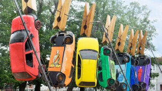 Seven cars hang from giant clothes pegs on a wire in Brighton as part of the annual Art Festival Fringe street theatre.