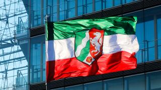 NRW North Rhine-Westphalia flag on flagpole blowing in the wind in front of the facade of the city gate, Dusseldorf, North Rhine-Westphalia, Germany