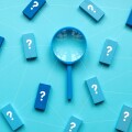 QnA or questions and answers concept. Blue magnifying glass with question symbol on wooden cube over a blue background.