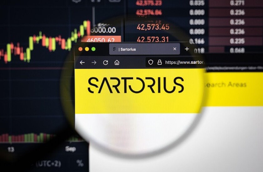 Sartorius company logo on a website with blurry stock market developments in the background, seen on a computer screen through a magnifying glass