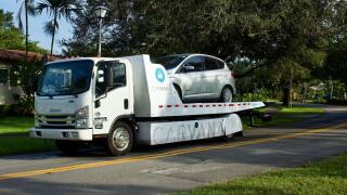 Carvana rollback delivery truck with Ford C-Max gas-electric hybrid in residential neighborhood