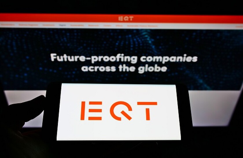 Person holding smartphone with logo of Swedish private equity firm EQT Partners AB on screen in front of website. Focus on phone display.